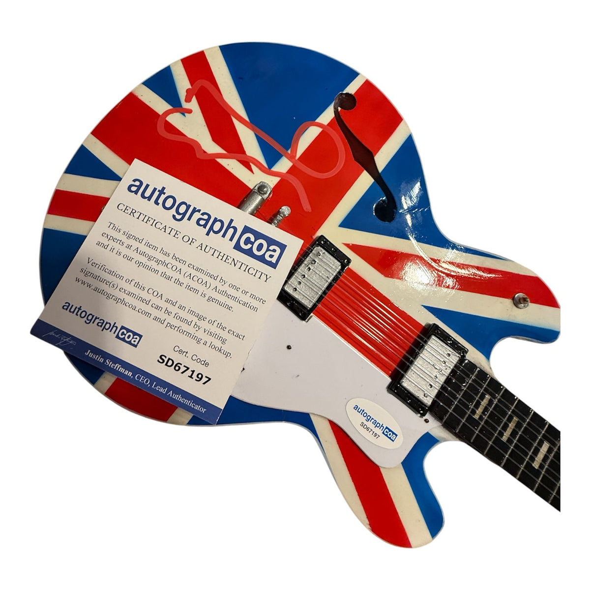 A high-resolution photo of an authentic Noel Gallagher signed union jack guitar, featuring the iconic British flag design with a bold, hand-signed autograph by the Oasis songwriter on the body with a certificate of authenticity (COA)