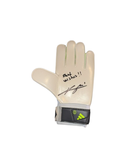 A professional-grade goalkeeper glove hand-signed by Arsenal's David Raya in silver permanent marker, displayed against a stadium backdrop.