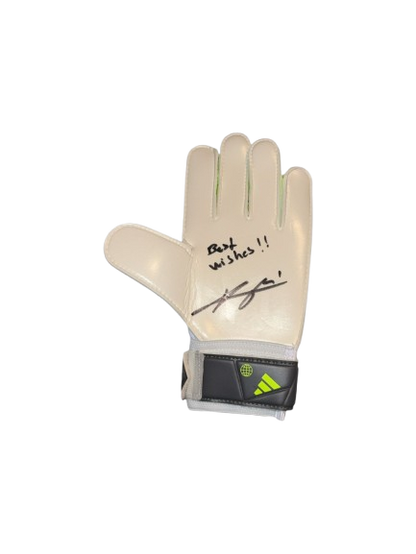 A professional-grade goalkeeper glove hand-signed by Arsenal's David Raya in silver permanent marker, displayed against a stadium backdrop.