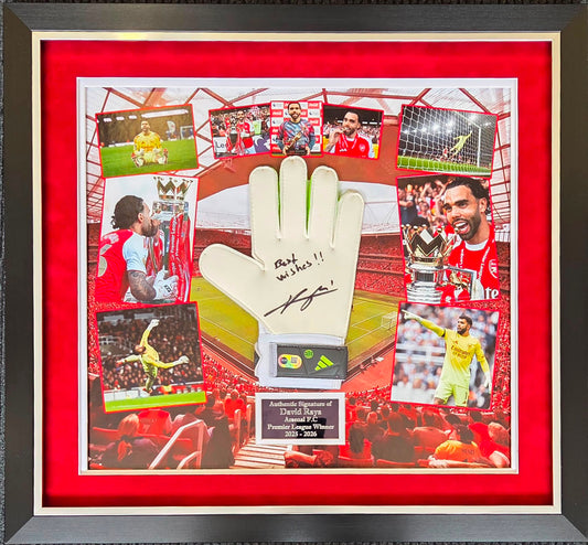 Front view of a sleek black frame containing a hand-signed David Raya goalkeeper glove with "best wishes" inscription, flanked by title celebration photos and an engraved plaque.