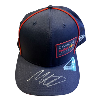 Detailed 45-degree top-down view of a genuine Max Verstappen autograph on the official navy Oracle Red Bull Racing team cap.