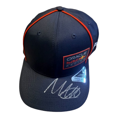A 45-degree display shot of a Max Verstappen signed Red Bull cap, highlighting the authentic driver branding and unique signature.