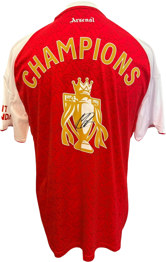 The reverse of the 2025/26 Arsenal home jersey showing the gold Champions print, featuring Martin Odegaard's hand-signed autograph directly on the printed Premier League trophy graphic.