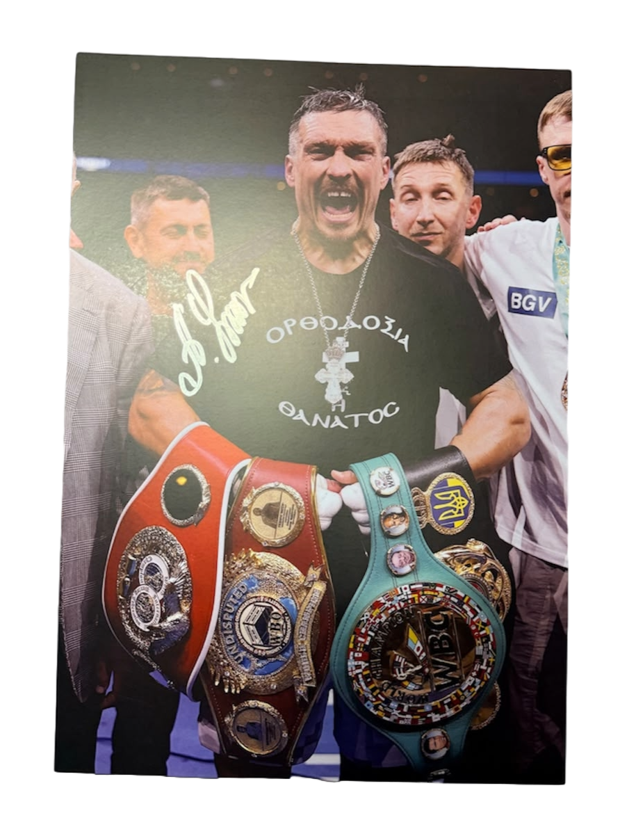 Signed Oleksandr Usyk photo posing proudly with all the undisputed heavyweight world title belts, featuring a bold hand-signed autograph across the image
