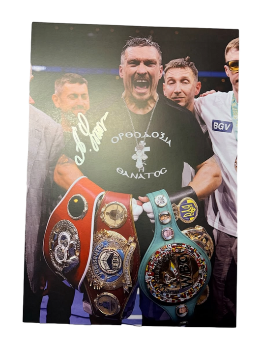 Signed Oleksandr Usyk photo posing proudly with all the undisputed heavyweight world title belts, featuring a bold hand-signed autograph across the image