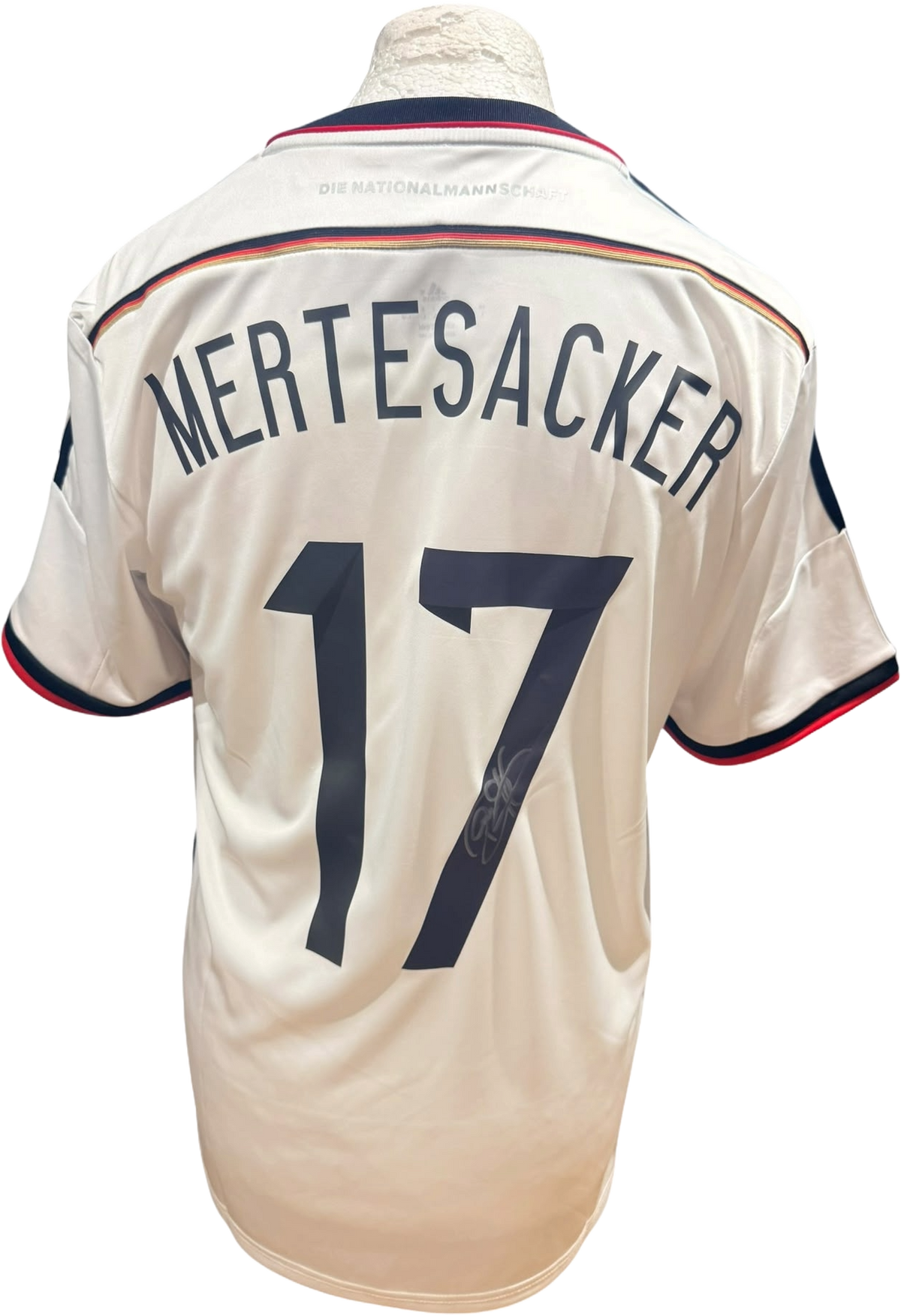 Rear view of a replica 2014 Germany home shirt hand-signed on the back by defender Per Mertesacker, displayed alongside the Certificate of Authenticity.