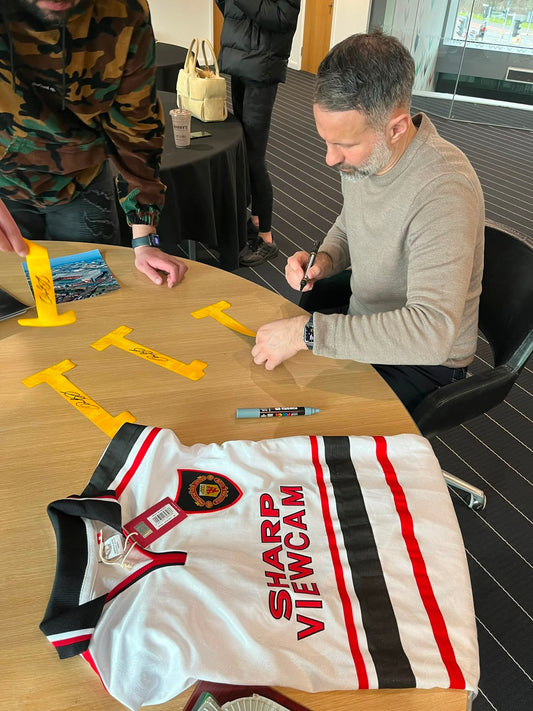 Ryan Giggs hand-signing a squad number on a Manchester United shirt alongside a personal dedication during an official signing session.