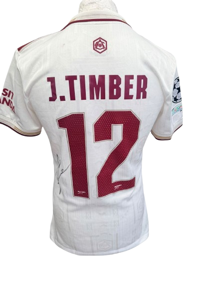Full-view of the hand-signed Jurrien Timber Arsenal 25/26 white third shirt displaying the official Champions League sleeve patches.