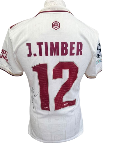 Full-view of the hand-signed Jurrien Timber Arsenal 25/26 white third shirt displaying the official Champions League sleeve patches.