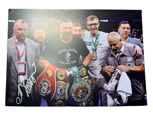 Signed Oleksandr Usyk landscape photo posing with the undisputed heavyweight world title belts, featuring a bold hand-signed autograph across the image