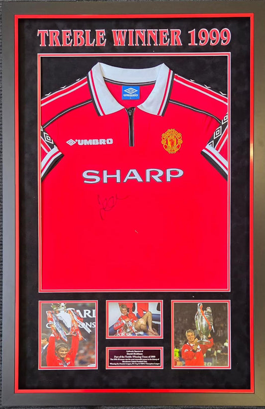Premium framed display containing a hand-signed Manchester United 1999 treble winners shirt by Sir David Beckham with commemorative imagery.