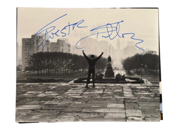 A hand-signed Sylvester Stallone photograph of Rocky Balboa standing at the top of the Philadelphia Museum of Art steps with arms raised.
